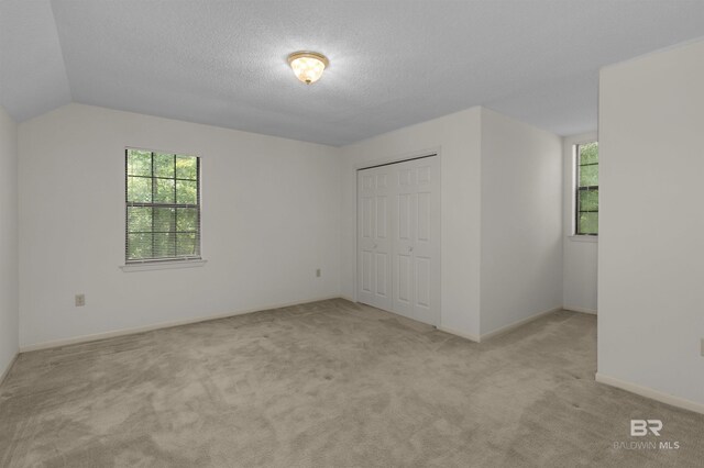 143 Kingswood Dr, Daphne, AL 36526 - unfurnished bedroom featuring multiple windows, carpet flooring, a closet, a textured ceiling, and vaulted ceiling