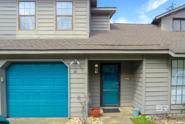 entrance to property featuring an attached garage and a shingled roof