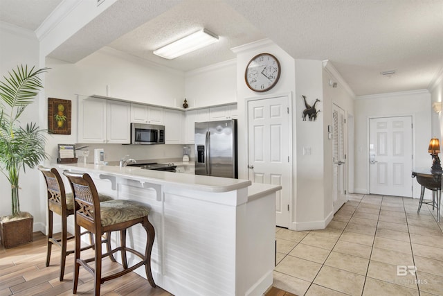 kitchen featuring crown molding, a textured ceiling, white cabinetry, kitchen peninsula, and stainless steel appliances