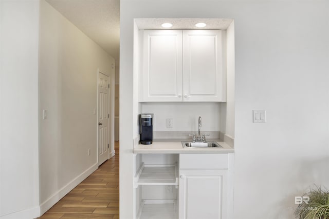 bar with a textured ceiling, light hardwood / wood-style floors, white cabinetry, and sink