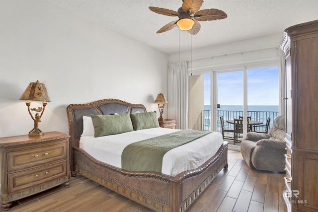 bedroom featuring a textured ceiling, a water view, dark hardwood / wood-style floors, and ceiling fan