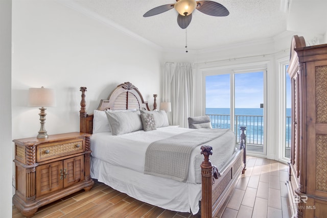 bedroom with a textured ceiling, access to outside, ceiling fan, a water view, and hardwood / wood-style flooring