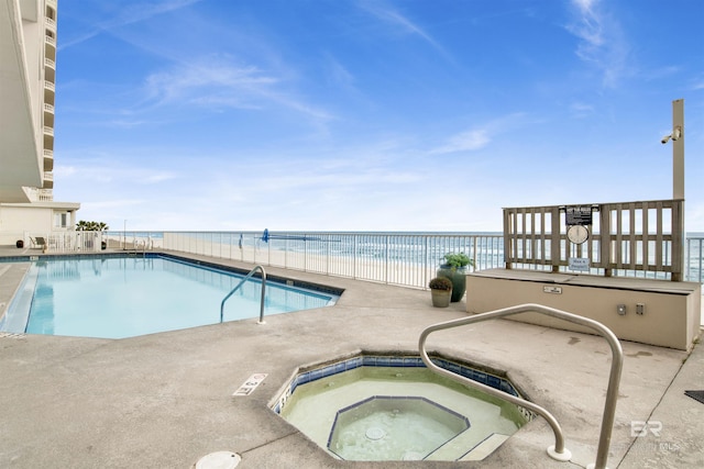 view of swimming pool with a water view, a view of the beach, and a hot tub