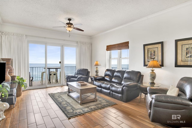 living room featuring a water view, light hardwood / wood-style flooring, ceiling fan, ornamental molding, and a textured ceiling