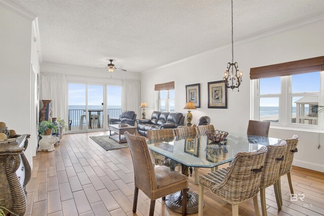 dining room with ceiling fan with notable chandelier, a water view, light hardwood / wood-style flooring, ornamental molding, and a textured ceiling