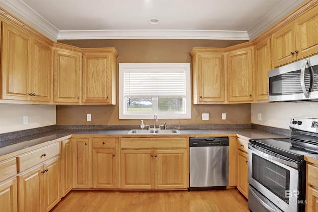 kitchen featuring appliances with stainless steel finishes, a sink, dark countertops, light wood-style floors, and crown molding