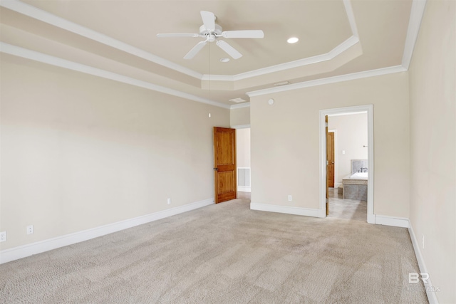unfurnished bedroom featuring a tray ceiling, light colored carpet, crown molding, baseboards, and connected bathroom