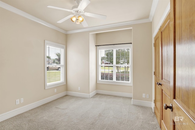 empty room featuring healthy amount of natural light, light carpet, crown molding, and baseboards