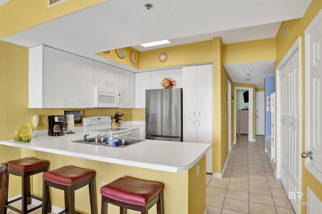 kitchen with kitchen peninsula, white appliances, white cabinetry, and a breakfast bar