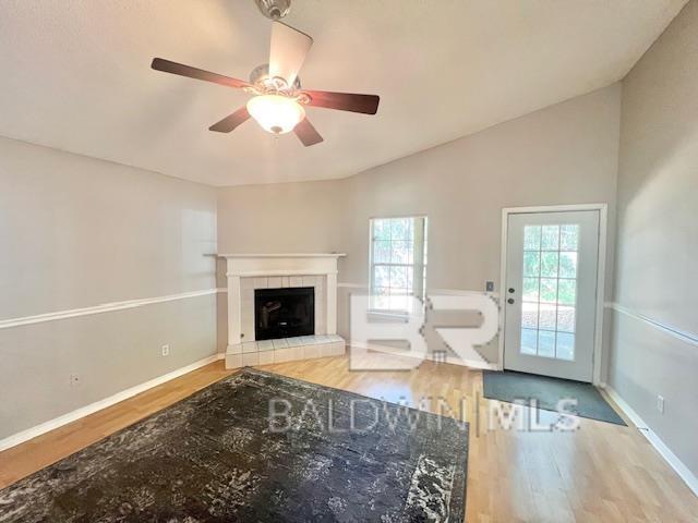 unfurnished living room featuring ceiling fan, wood-type flooring, a tiled fireplace, and vaulted ceiling