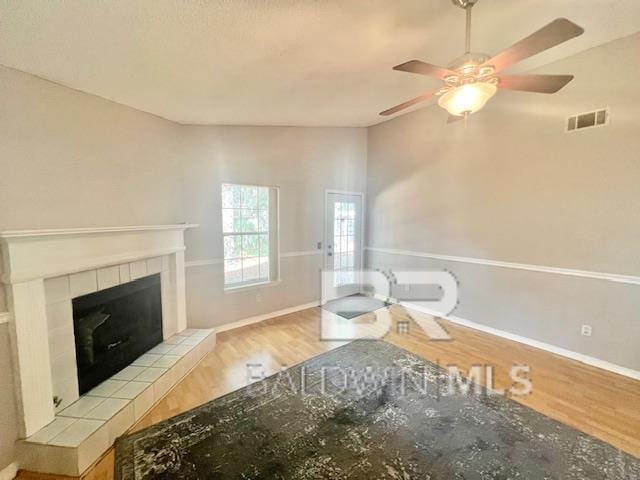 unfurnished room featuring ceiling fan, a tile fireplace, and light wood-type flooring