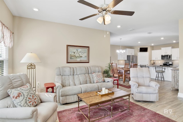 living room with ceiling fan with notable chandelier and light wood-type flooring