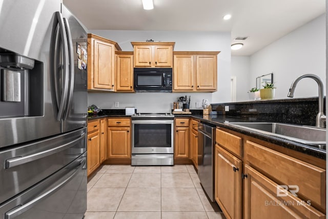 kitchen featuring dark stone counters, appliances with stainless steel finishes, light tile patterned flooring, and a sink