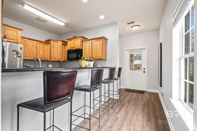 kitchen with black microwave, a peninsula, visible vents, light wood-type flooring, and freestanding refrigerator