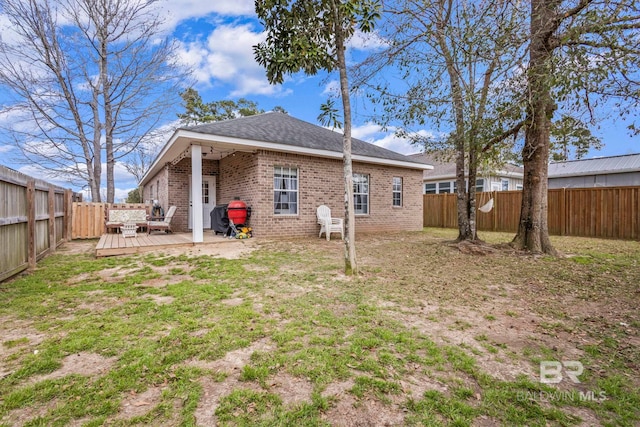 back of property featuring brick siding, a lawn, a fenced backyard, and a wooden deck