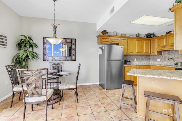 kitchen with a sink, freestanding refrigerator, visible vents, decorative backsplash, and light stone counters