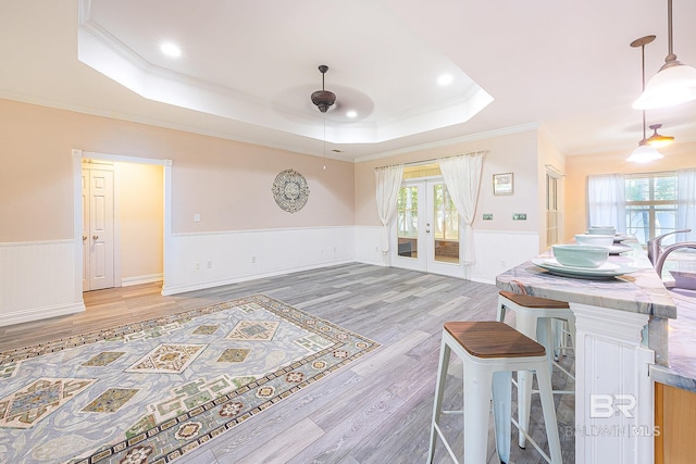 living room with french doors, ornamental molding, a tray ceiling, and light hardwood / wood-style floors