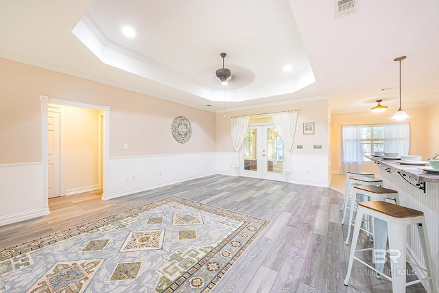 living room with crown molding, a tray ceiling, wood-type flooring, and a healthy amount of sunlight