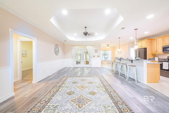 kitchen with appliances with stainless steel finishes, a kitchen bar, a tray ceiling, light brown cabinets, and french doors