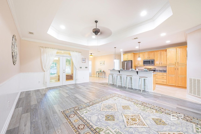 kitchen with light brown cabinetry, a center island with sink, appliances with stainless steel finishes, a kitchen breakfast bar, and a raised ceiling