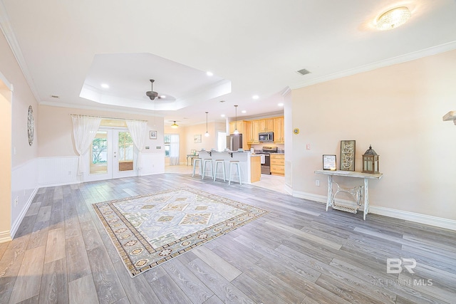 unfurnished living room featuring french doors, crown molding, a tray ceiling, and light hardwood / wood-style flooring