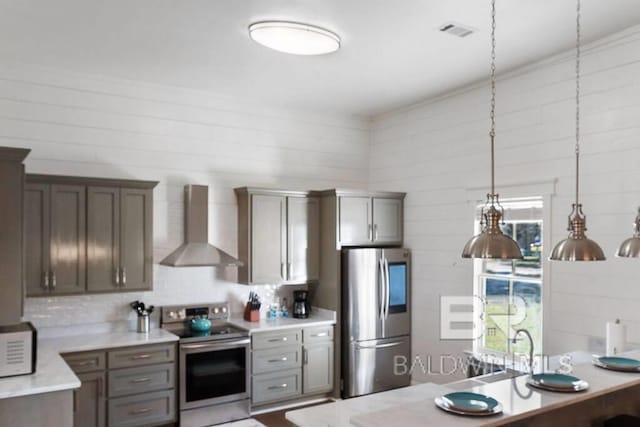 kitchen with pendant lighting, wall chimney range hood, appliances with stainless steel finishes, and tasteful backsplash