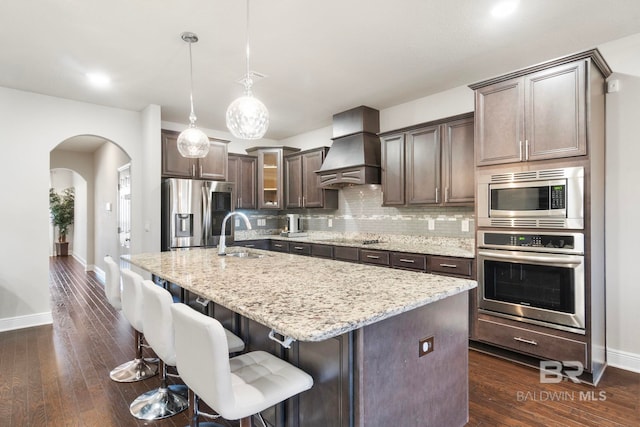 kitchen featuring sink, hanging light fixtures, premium range hood, a kitchen island with sink, and appliances with stainless steel finishes