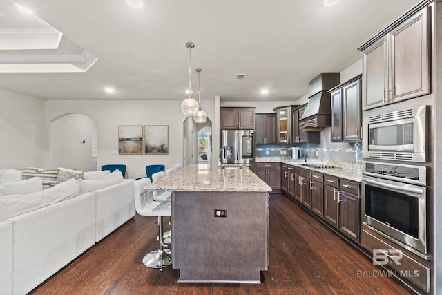 kitchen featuring dark brown cabinetry, backsplash, an island with sink, appliances with stainless steel finishes, and custom exhaust hood