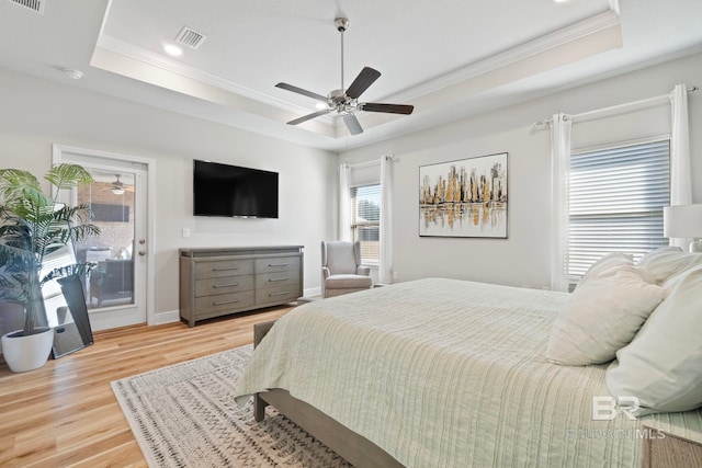 bedroom featuring access to exterior, a tray ceiling, light hardwood / wood-style flooring, and ceiling fan