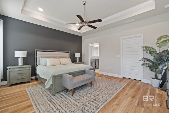 bedroom with a raised ceiling, ensuite bath, ceiling fan, and light hardwood / wood-style flooring