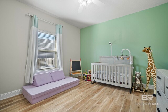 bedroom featuring ceiling fan, light hardwood / wood-style flooring, and a crib