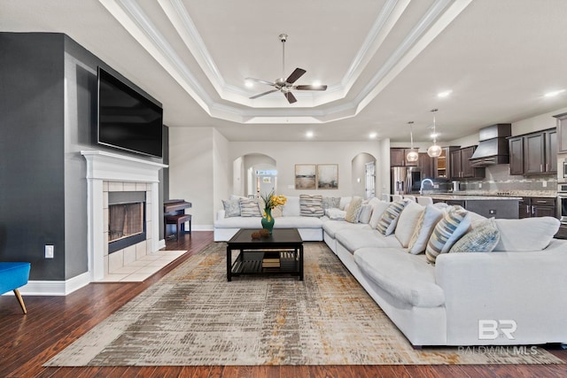 living room with ceiling fan, wood-type flooring, crown molding, and a tile fireplace