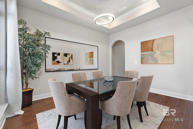 dining room with ornamental molding, a tray ceiling, and dark wood-type flooring