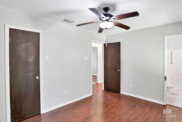 unfurnished bedroom featuring ensuite bath, ceiling fan, and dark wood-type flooring