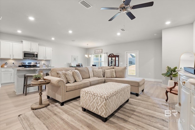 living room with ceiling fan with notable chandelier and light hardwood / wood-style flooring