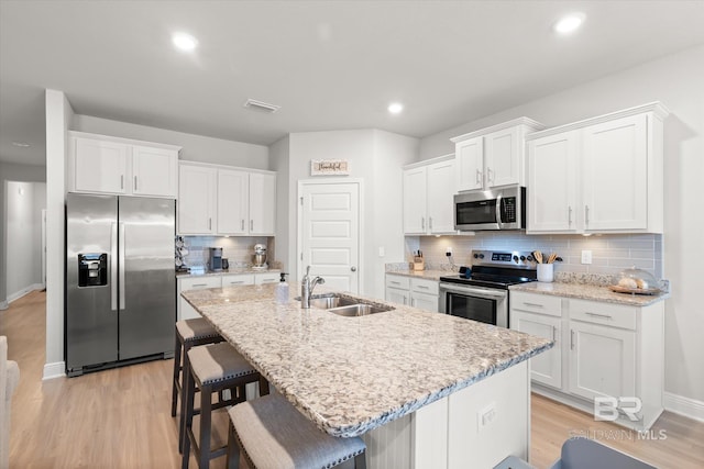 kitchen with a kitchen bar, an island with sink, stainless steel appliances, white cabinets, and sink