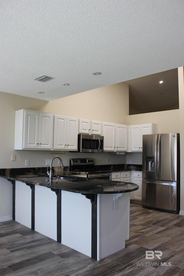 kitchen with kitchen peninsula, stainless steel appliances, dark hardwood / wood-style flooring, high vaulted ceiling, and white cabinets