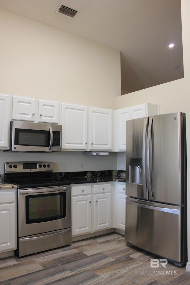 kitchen with a high ceiling, hardwood / wood-style floors, white cabinets, and appliances with stainless steel finishes