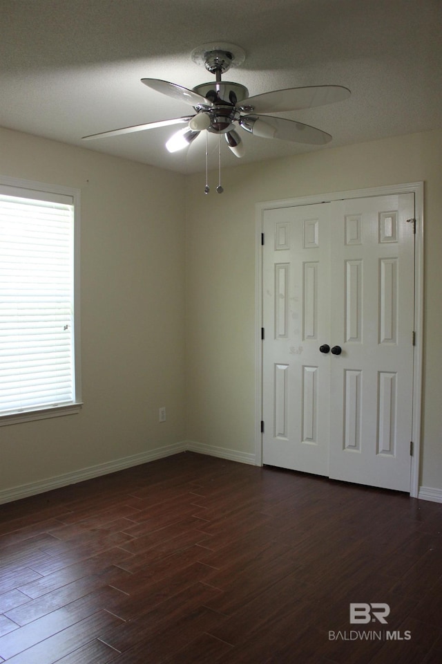 unfurnished bedroom with ceiling fan, a closet, and dark wood-type flooring