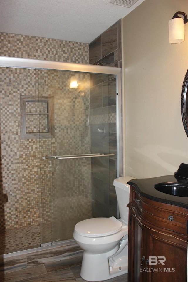 bathroom with vanity, toilet, a textured ceiling, and a shower with door