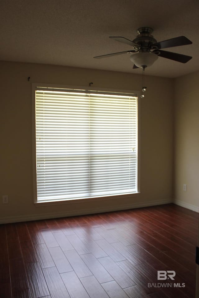 empty room with a healthy amount of sunlight, dark wood-type flooring, and ceiling fan