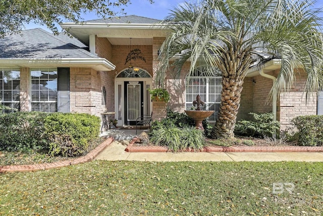 entrance to property with brick siding and a shingled roof