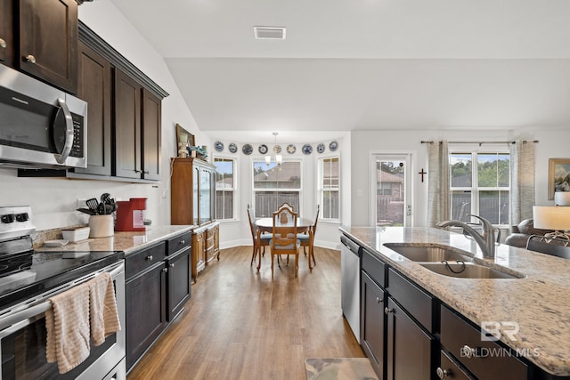 kitchen with sink, vaulted ceiling, dark brown cabinets, light stone counters, and stainless steel appliances