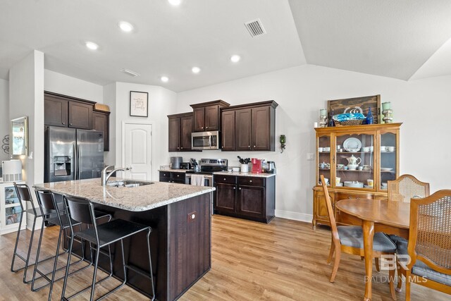 kitchen featuring light stone countertops, appliances with stainless steel finishes, a breakfast bar, sink, and a center island with sink