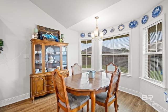 dining room with light wood-type flooring, an inviting chandelier, vaulted ceiling, and plenty of natural light