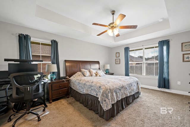 bedroom with light colored carpet, a raised ceiling, and ceiling fan