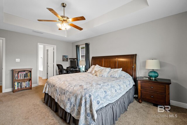 bedroom featuring a raised ceiling, ceiling fan, and light carpet