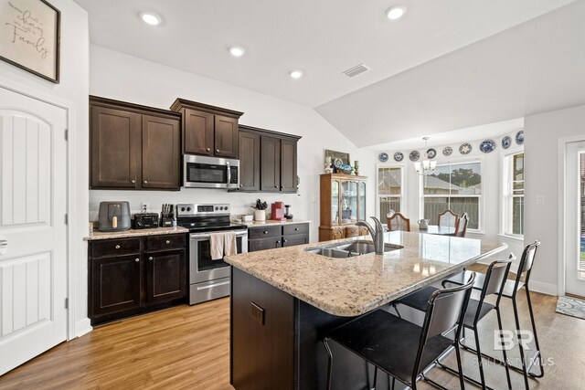 kitchen with a kitchen island with sink, sink, light wood-type flooring, and appliances with stainless steel finishes