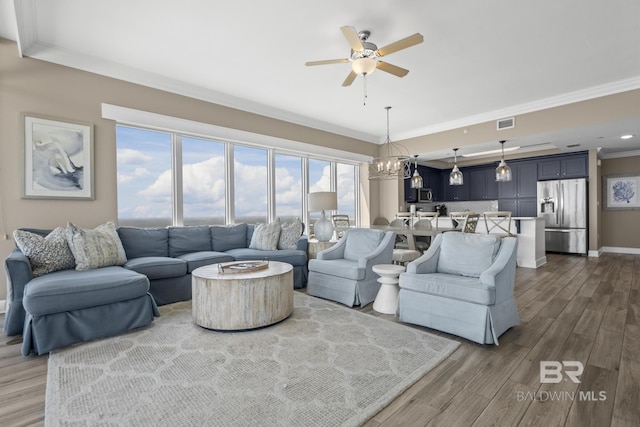 living room featuring crown molding, wood-type flooring, and ceiling fan with notable chandelier