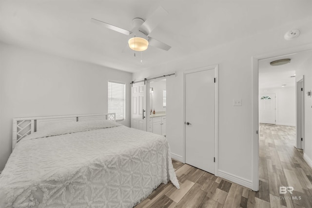 bedroom with a barn door, ceiling fan, ensuite bathroom, and light hardwood / wood-style floors